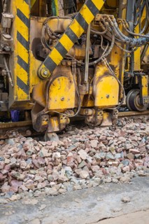 Large construction machine in use. Gravel and yellow-black markings visible, tamping machine on