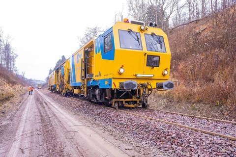 Yellow working trains on railroad tracks in a wintry landscape with gravel, stuffing machine on