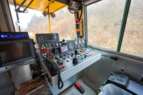 Interior view of a train driver's cab with numerous switch and control buttons, stuffing machine on