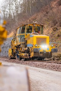 Yellow track construction equipment on tracks with wooded track under construction, tamping machine