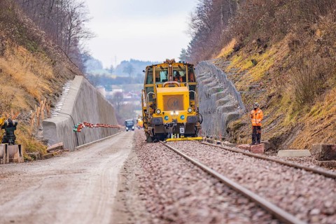 Rail construction machine in the landscape, workers seen along the tracks, tamping machine on
