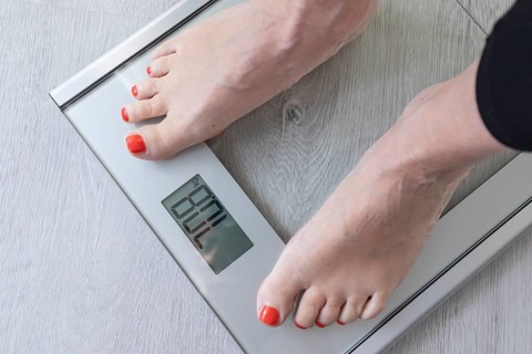 Feet of a woman standing on a digital bathroom scale while monitoring her weight. This scene