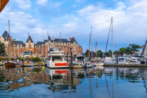 Luxury yachts and sailboats are moored in front of the fairmont empress hotel, reflecting in the