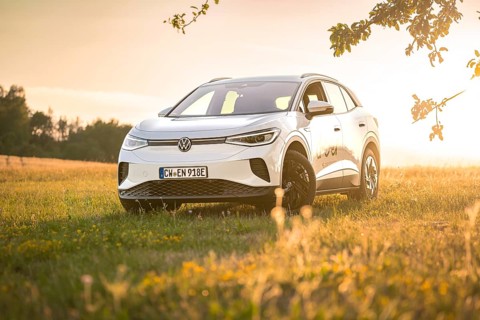 White car standing in a field in warm sunlight at sunset surrounded by grass, VW ID4 electric car,