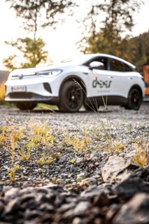 White car photographed from a blurred perspective on rocky ground with plants in the foreground, VW
