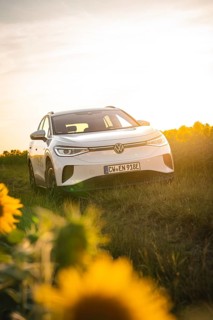 A white car is parked in a meadow near sunflowers at sunset, VW ID4 electric car, Deer Carsharing,