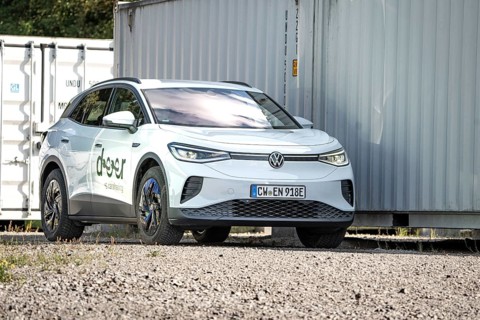 White car parked in a rocky place next to large metal containers, modern ambiance, VW ID4 electric