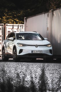 A car on a gravel field next to stacked containers in the shade, VW ID4 electric car, Deer