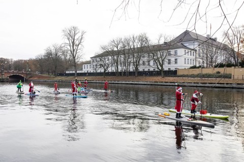 Water sports enthusiasts dressed up as Santa Claus ride SUPs on the Spree in front of Bellevue
