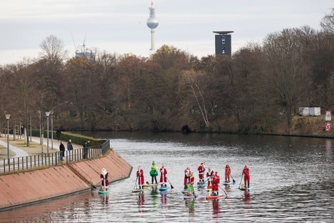 Water sports enthusiasts dressed up as Santa Claus ride SUPs on the Spree am Park at the