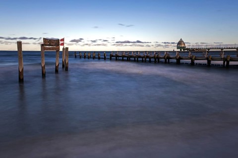 Wooden sign in the sea with inscription Zingst and wooden walkway, pier with diving gondola behind,