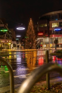 Large illuminated Christmas tree surrounded by colorful street lights in rainy city at night,