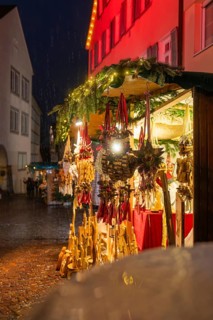 Sales stand at the Christmas market with wooden decorations and lights in the rain at night,