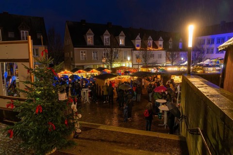 Christmas market at night, lots of visitors with umbrellas, Christmas tree and bright lights,