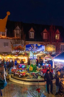 Families in front of an illuminated carousel with toys at a night-time Christmas market, Böblingen