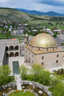 Mosque with golden dome and surrounding garden, nestled in a hilly landscape, Rabati Fortress,