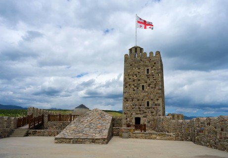 Stone castle with tower and Georgian flag on a plateau under cloudy sky, Rabati Fortress,