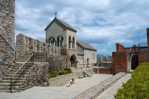 Stone complex with stairs, a church entrance and an open courtyard under cloudy sky, Rabati