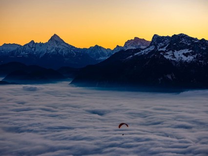 Paragliding flies over a sea of fog, behind Berchtesgaden Alps with Watzmann, Hochkalter and