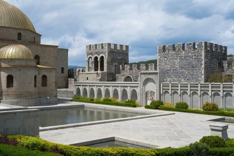 Stone building with golden dome, arcades and water basin in front of an imposing stone wall, Rabati