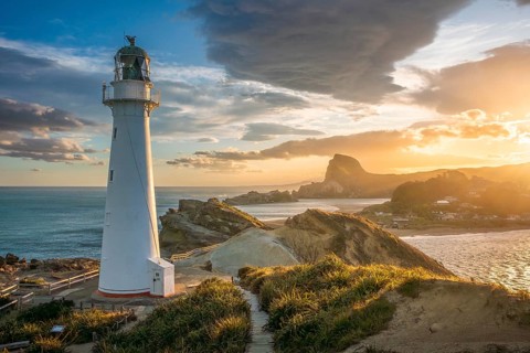 The Castlepoint lighthouse on a rock, ocean, Deliverance Cove and Castle Rock in the background.