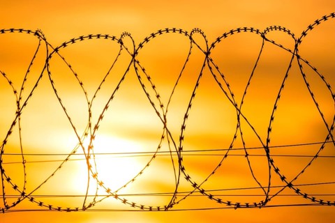 Barbed wire against a dramatic orange sky at sunset conveys an atmosphere of borders and