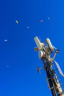 Paragliders with colored paragliders fly over the transmitter and cell phone tower at the summit of