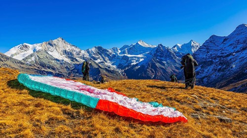 Paragliders are preparing for their start, with the snow-capped peaks of the Valais Alps, Val