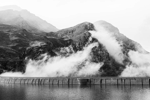 Fog rises over the dam of the Lac de Moiry reservoir, black and white photo, Val d'Anniviers,