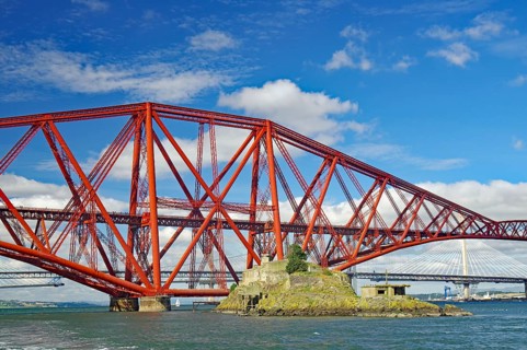 A large, red bridge stretches over water, on which a small island lies, fortification from the