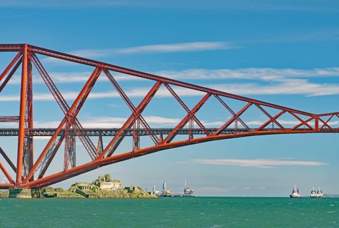 A section of a red bridge over a lake with passing boats, railway bridge, Firth of Forth,