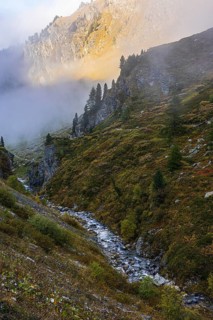 Small stream flows from Lac de Moiry reservoir to Grimentz, mountain slopes in the evening light,
