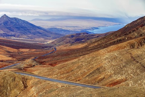Road leads through the mountainous landscape of Fuerteventura with extensive views over the sea,