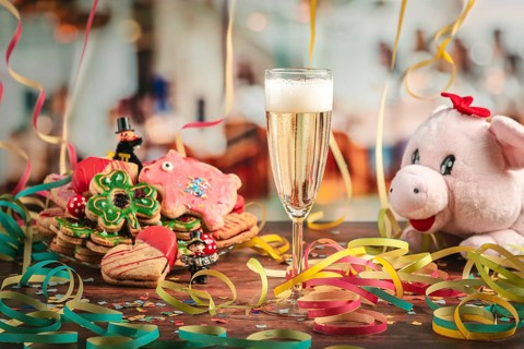 Filled champagne glass surrounded by New Year cookies, streamers and plush pig
