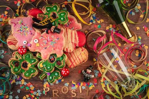 New Year cookies, confetti and prosit lettering next to champagne bottle