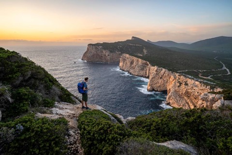 Tourist in front of coastal landscape at sunset, steep cliffs by the sea, cliffs in the evening