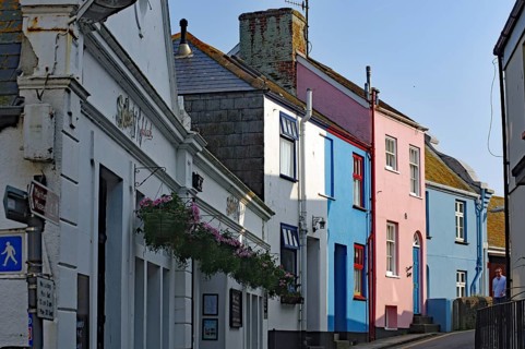 Colourful houses line a narrow village street under clear skies, Cornwall, United Kingdom