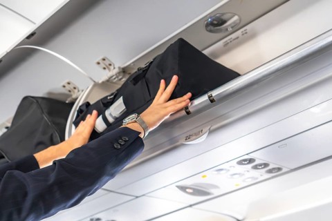 Businessman wearing suit and watch is storing hand luggage in the overhead compartment of a