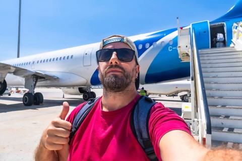 Happy bearded tourist wearing sunglasses and backpack taking selfie showing thumbs up gesture while