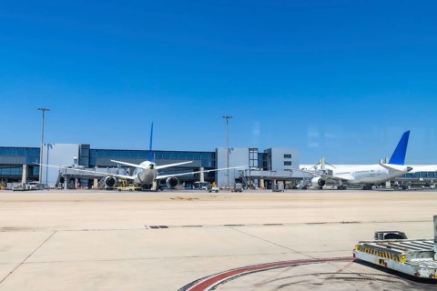 Two large passenger airplanes parked at airport gates under a bright sunny sky, waiting for