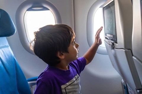 Young boy enjoying his first flight, gazing out the window with wonder and touching the screen on