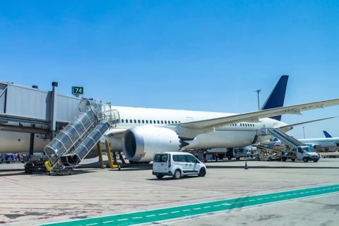 Modern passenger airplane parked at airport gate, connected to jet bridge, with ground crew and