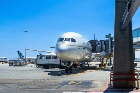 Wide body airplane connected to a jet bridge at an airport gate, ground crew preparing for