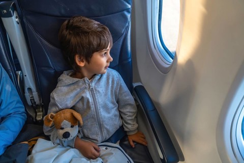Curious child traveling by plane, clutching a plush toy while gazing out the window, marveling at