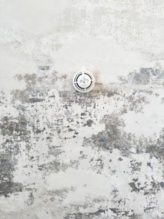 Round ceiling sprinkler nozzle in minimalistic concrete ceiling with chipped paint and abstract