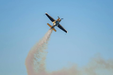 Golden stunt aerobatic plane performing stunts in blue sky with smoke trail. Concept of speed,