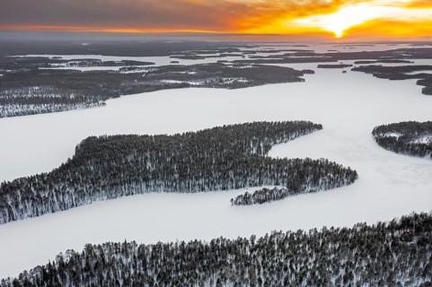 Aerial view over forest and snow covered frozen Lahnaselkä lake in Kuusamo in winter, Koillismaa,