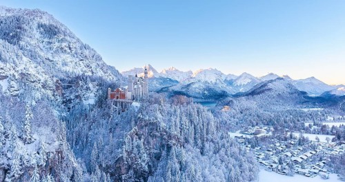 Neuschwanstein Castle is perched in the snowy alpine landscape, surrounded by peaceful forests