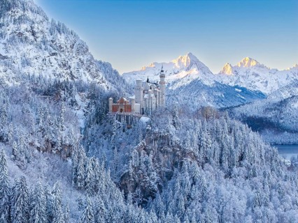 Neuschwanstein Castle surrounded by mountains in snow, in the warm light of sunrise, Schwangau near