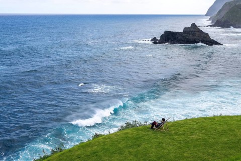Woman sitting comfortably in deckchair in a meadow and watching waves in the sea, Madeira, Portugal
